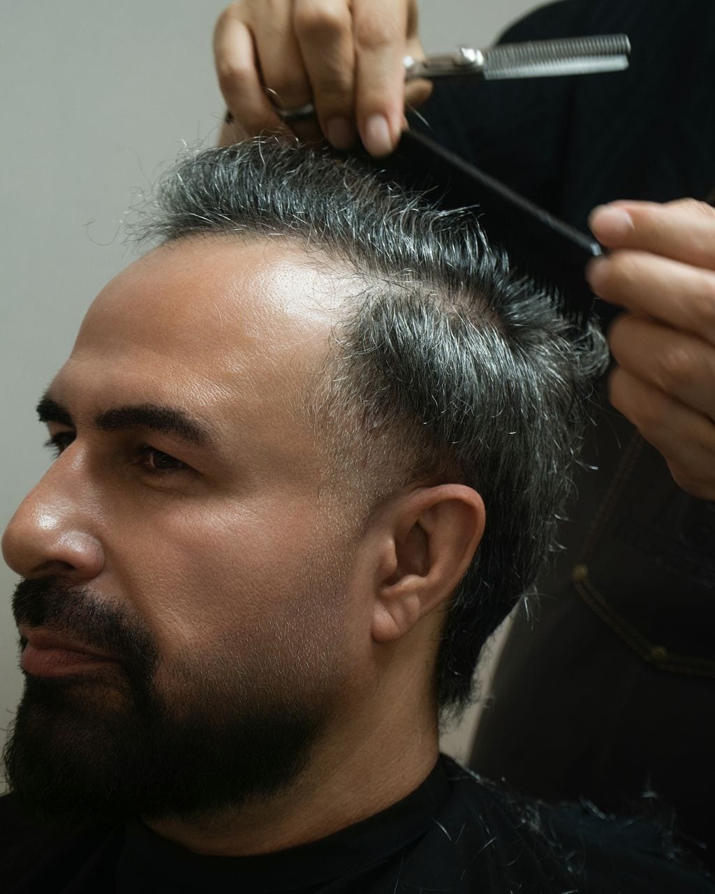 Client in profile while his hair is shaped with comb and scissors