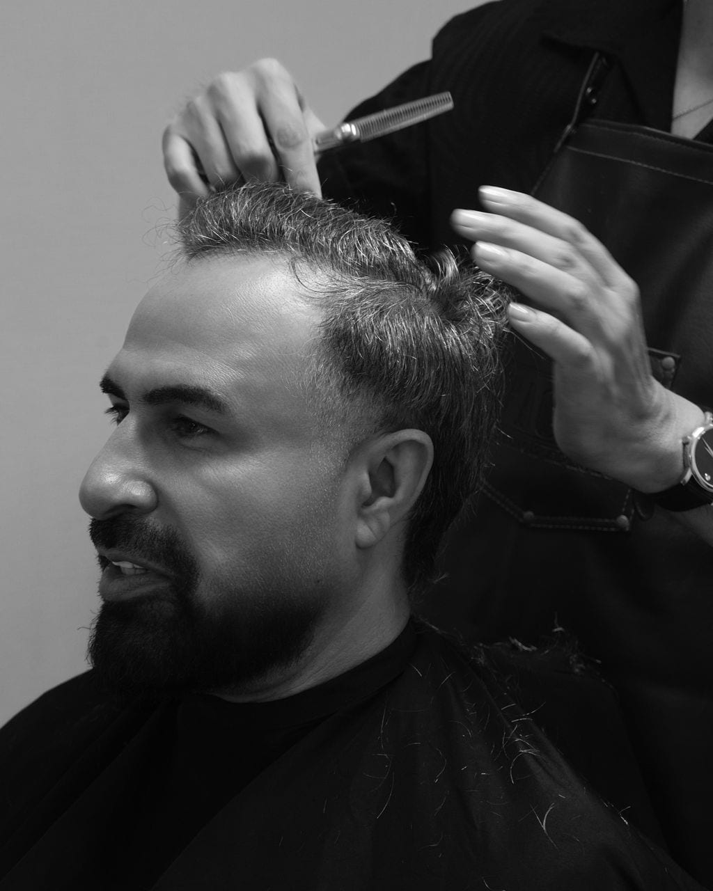 Black and white profile of a client while hands shape his hair