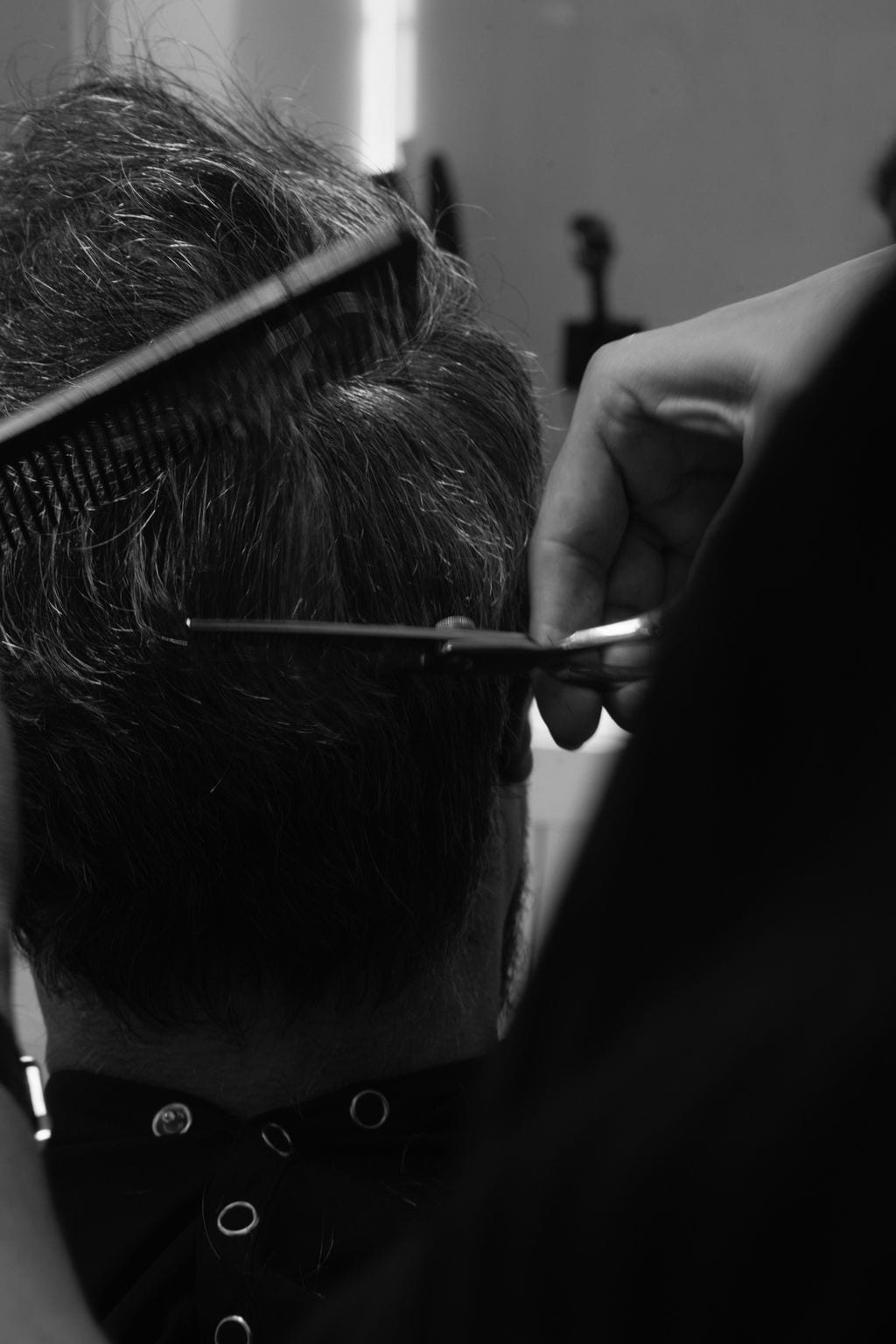 Black and white detail of scissors and comb working through dark hair